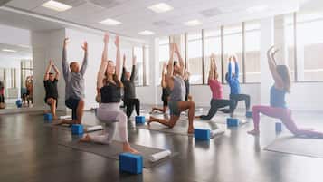 A group of people in a spacious room with large windows, performing a yoga class.