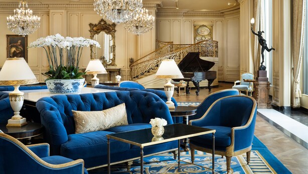 A luxurious room with a grand piano, plush blue sofas, ornate chandeliers, and elegant decor. - Westgate Hotel (San Diego)