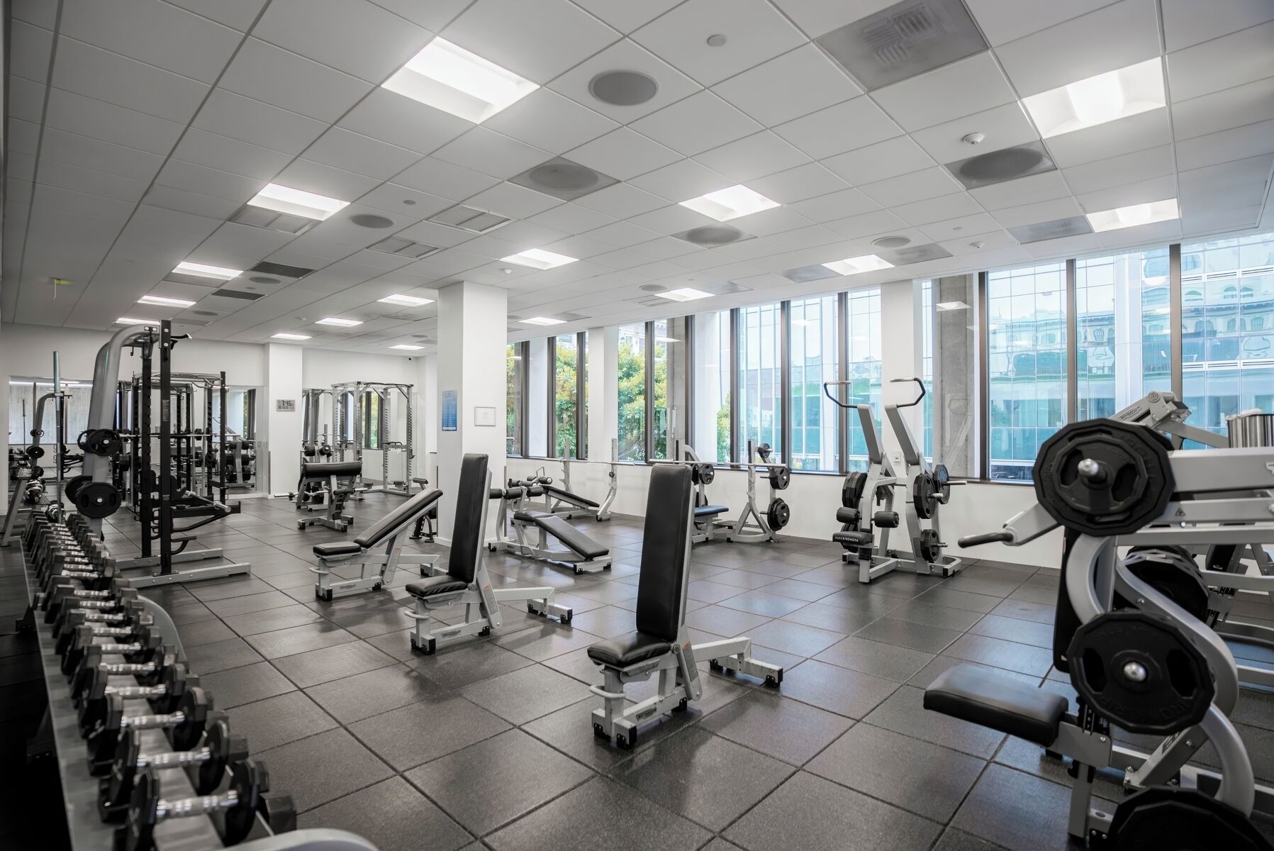 A gym with various exercise equipment, large windows, and a tiled floor.