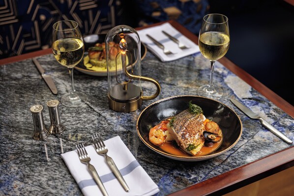 A dining table with a seafood dish, wine glasses, cutlery, and a decorative light.