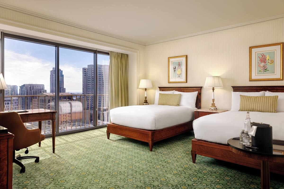 Quarto de hotel com duas camas, uma escrivaninha e uma cadeira.