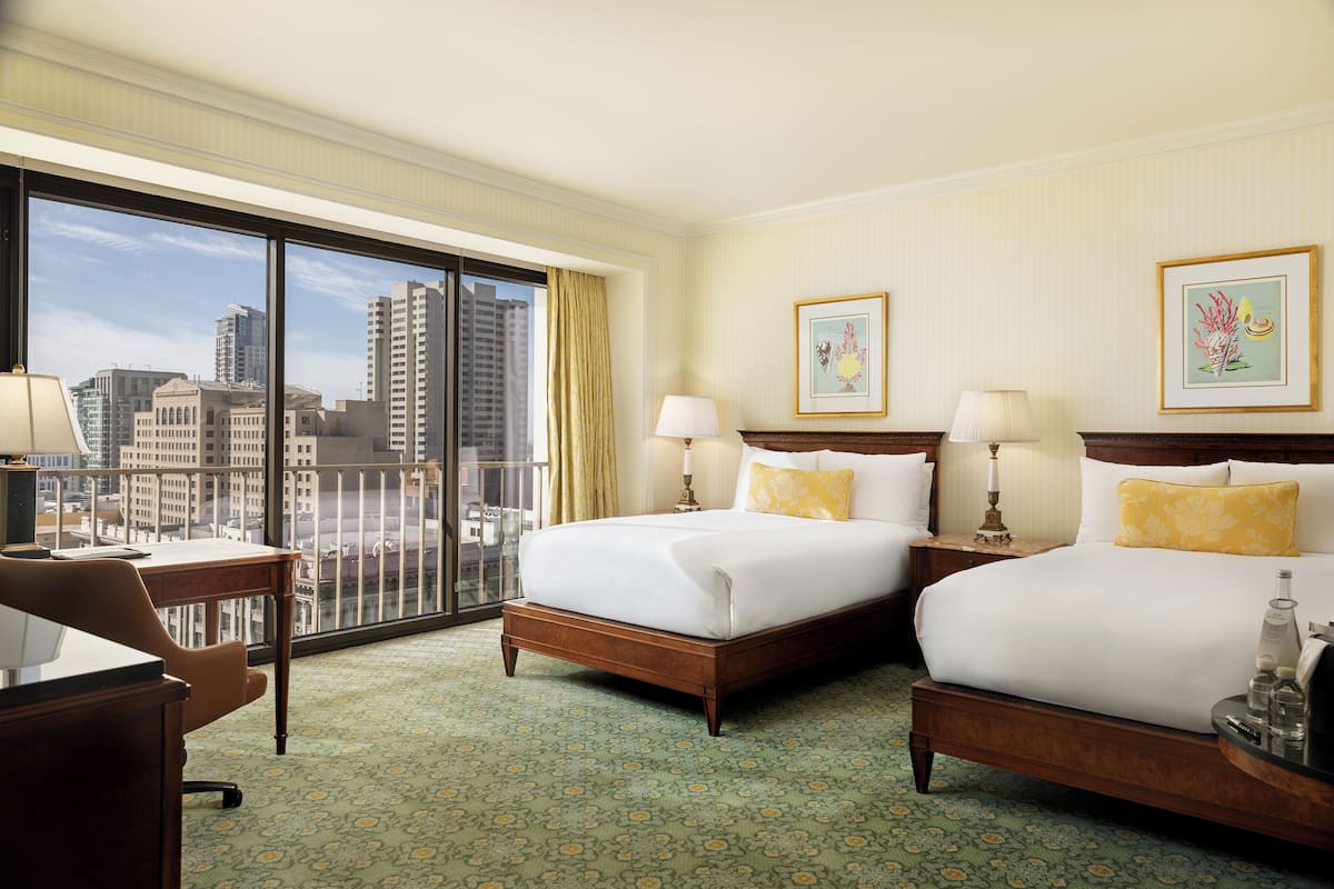 Quarto de hotel com duas camas, uma escrivaninha e vista para a cidade.