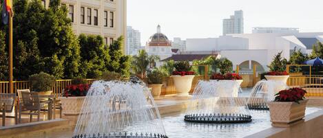 A fountain with multiple water jets in a courtyard with seating and potted plants.
