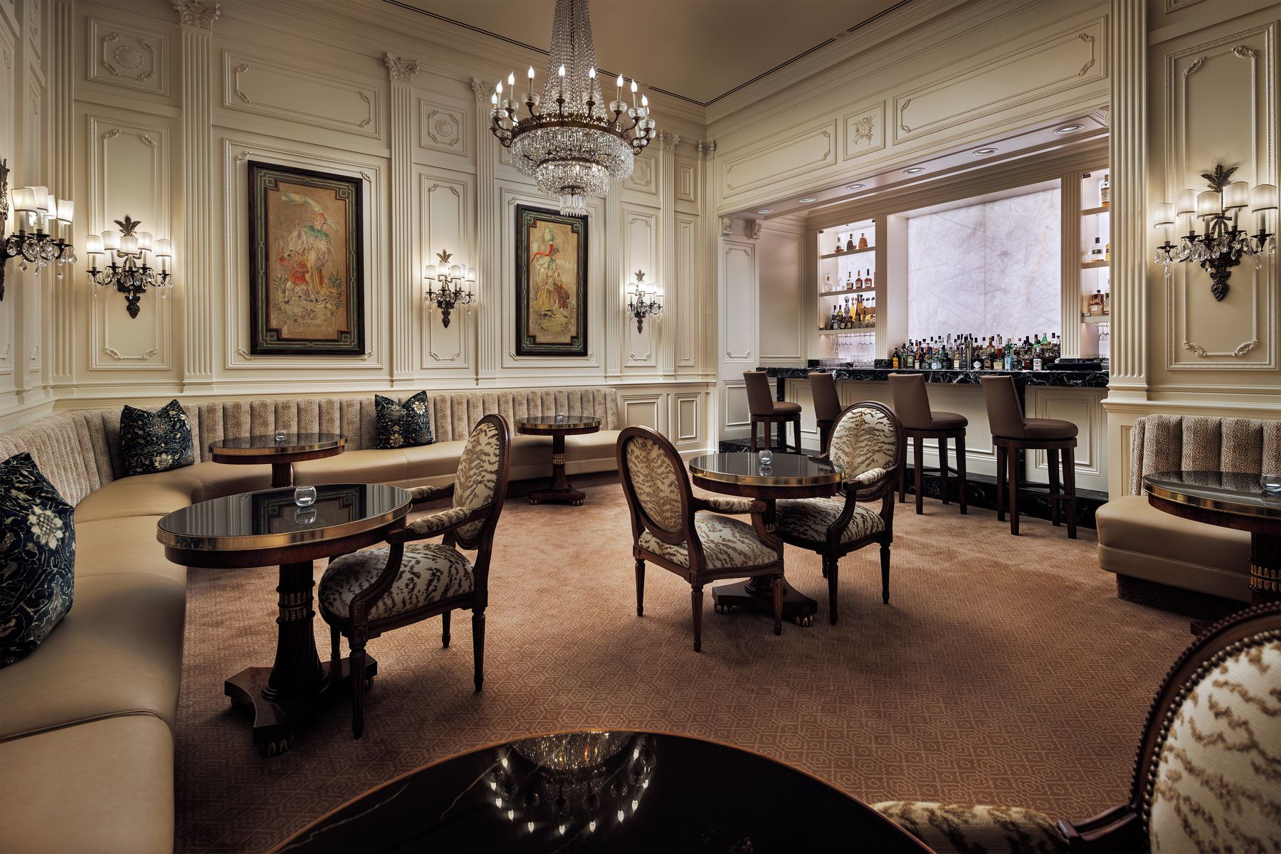 A luxurious hotel lobby with ornate chandeliers, a bar area, and comfortable seating arrangements.