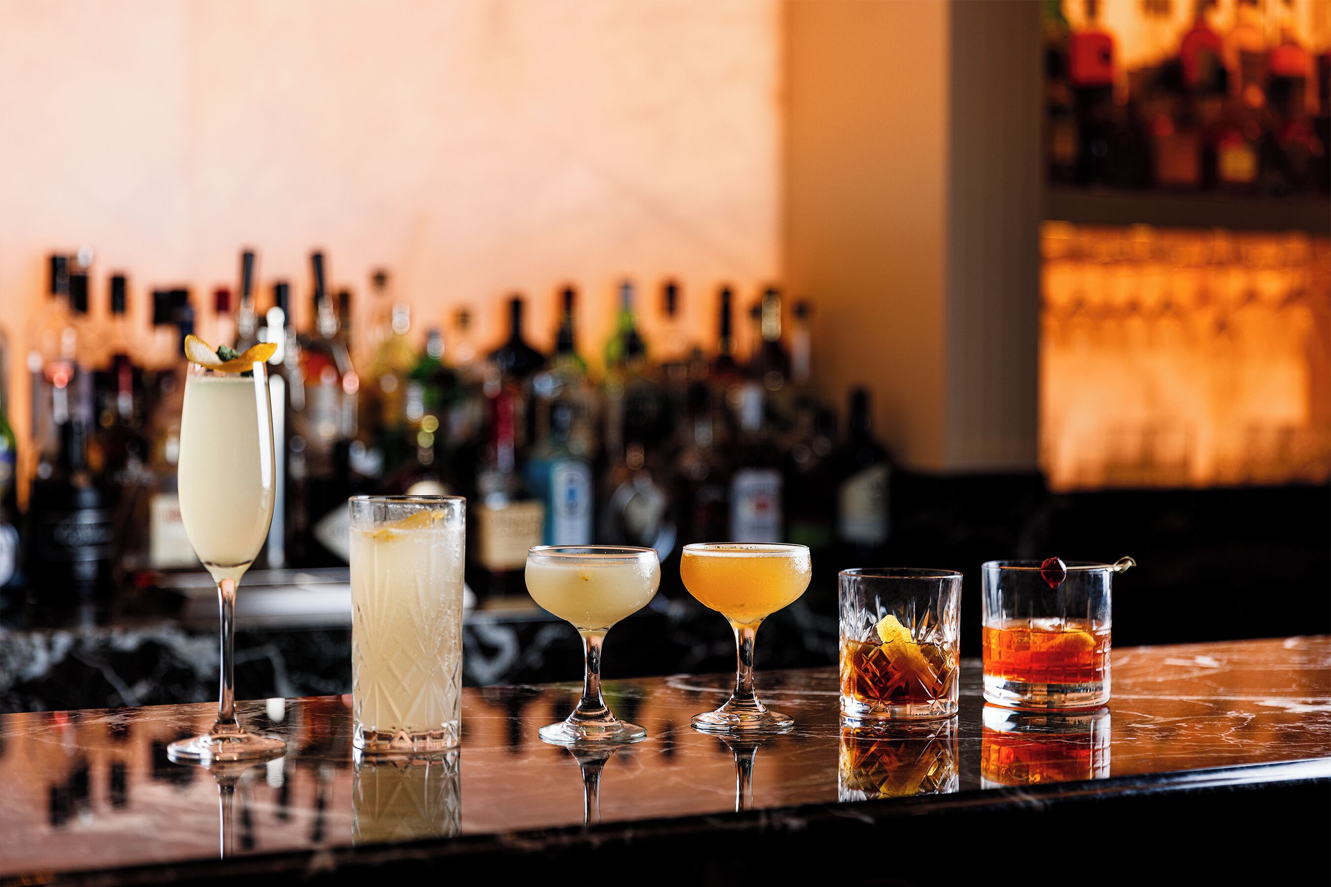 Um bar com diversos cocktails e garrafas ao fundo.