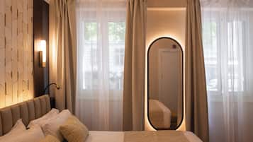 Ein Hotelzimmer mit einem Bett, einer Wandleuchte, einem Spiegel und durchsichtigen Vorhängen.