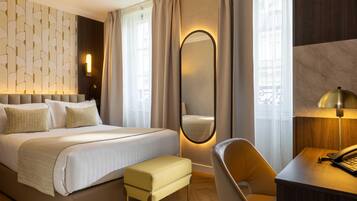 A modern hotel room with a bed, a desk, a chair, a mirror, and a wall with a geometric pattern.