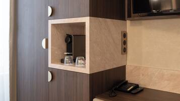 Une pièce de taille modeste, dotée d’une armoire en bois, d’un petit miroir, d’un téléviseur fixé au mur et d’un bureau avec une chaise.
