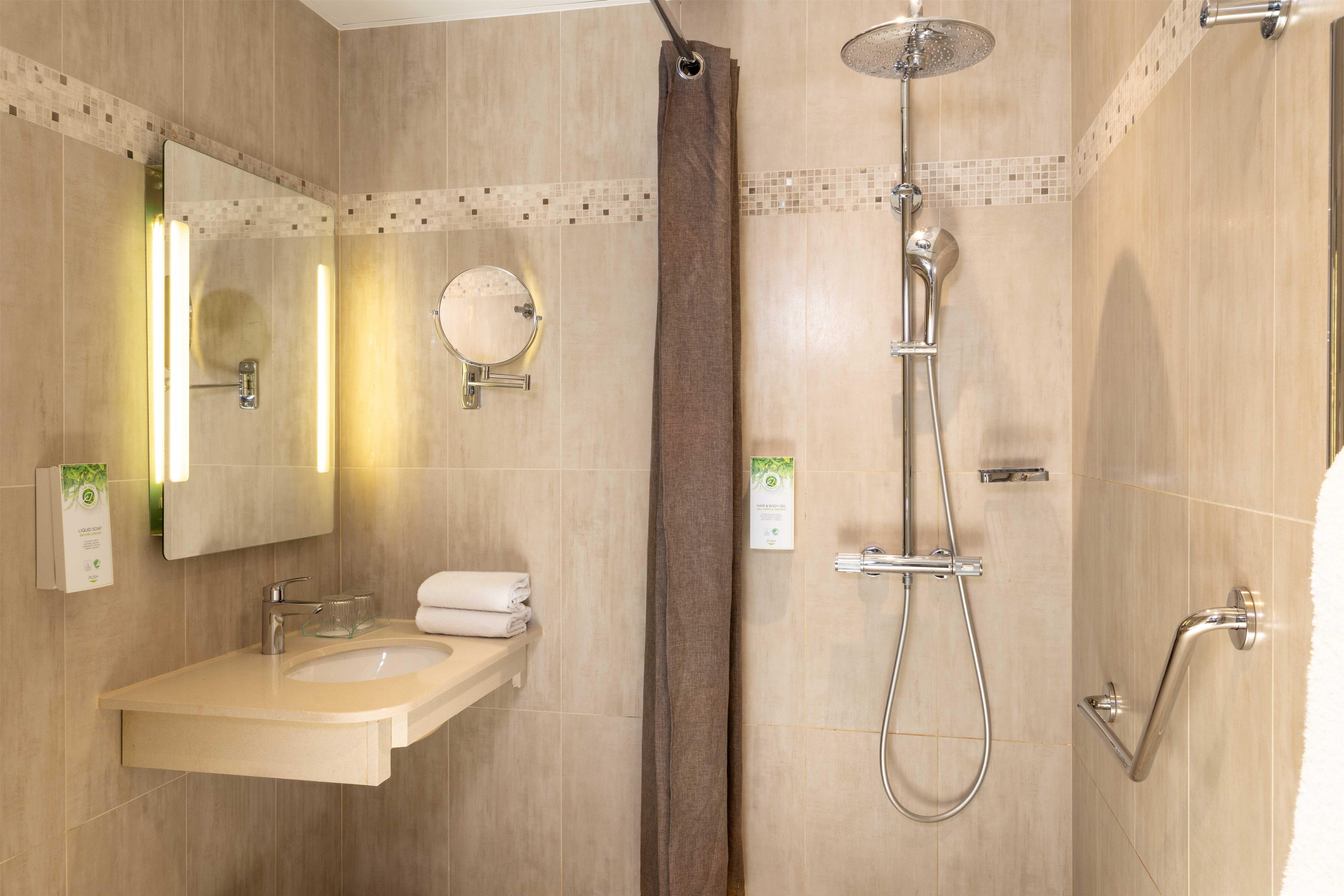 Un baño con lavamanos, espejo, toallero, ducha y una toalla colgada en la pared.
