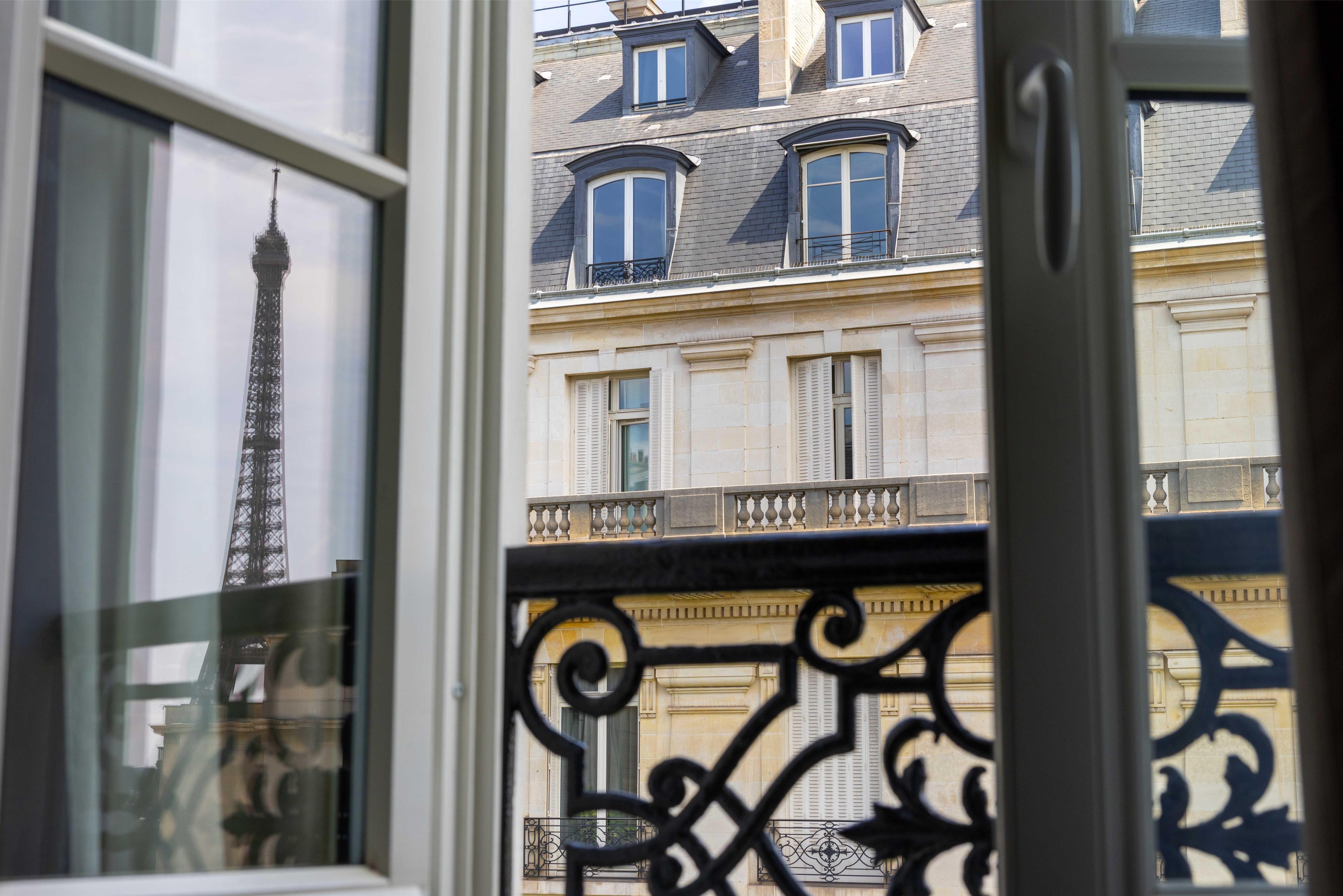 A view of a building with multiple windows and balconies, a metal railing, and a glimpse of the Eiffel Tower in the background.