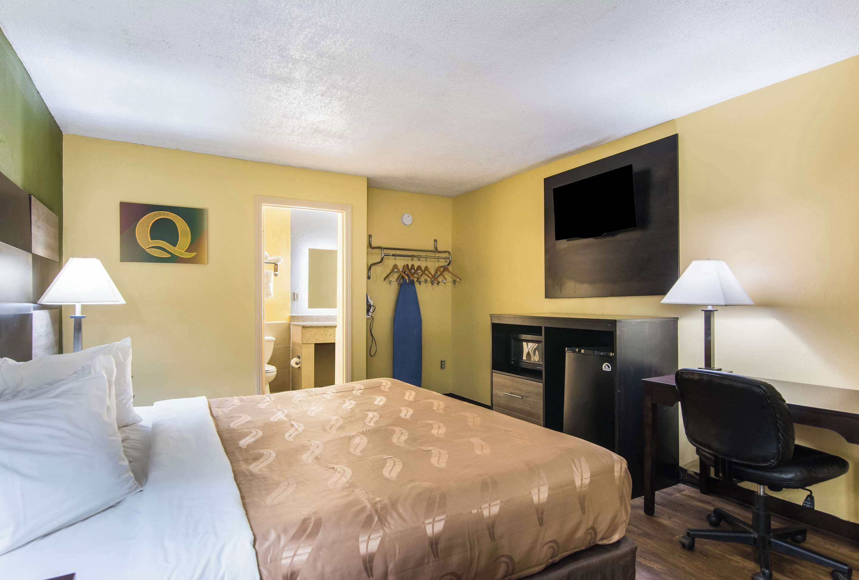A hotel room with a bed, desk, chair, TV, and a coat rack.