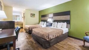 Une chambre d’hôtel avec deux lits, un bureau, une chaise, une lampe et un mur vert.