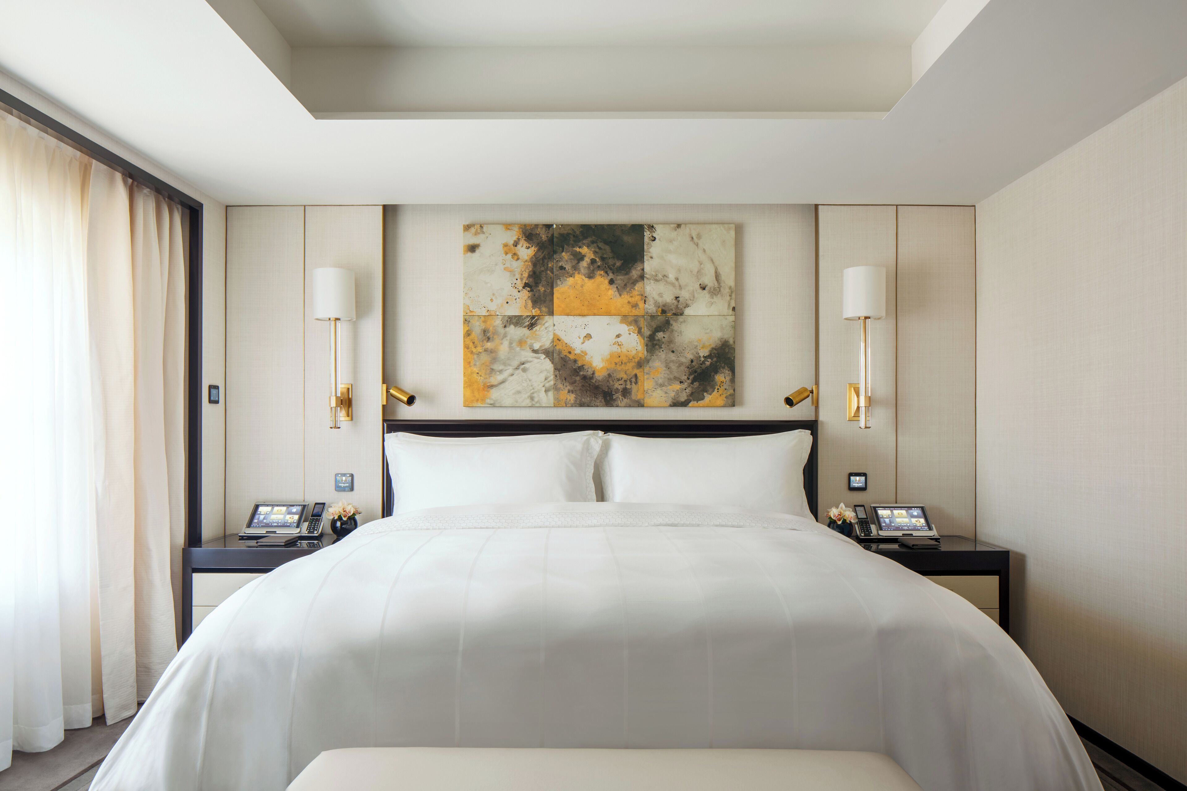 Una habitación de hotel con una cama grande, dos mesitas de noche, una obra de arte en la pared y una ventana con cortinas.
