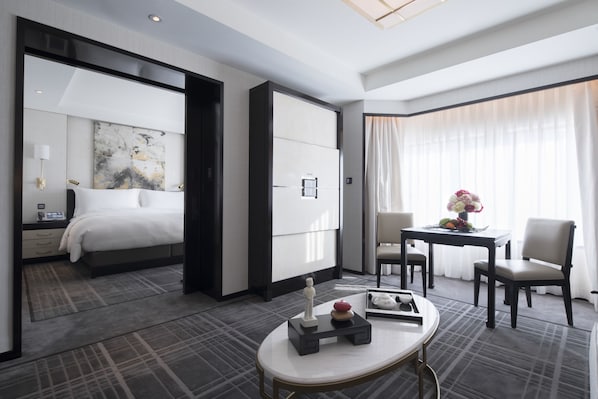Une chambre d’hôtel moderne, dotée d’un grand lit, d’un bureau agrémenté d’un vase de fleurs et offrant une vue sur la ville grâce à de grandes fenêtres.