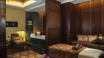 A hotel room with a spa area, including a bathtub, a sofa, and a bed with a decorative headboard.