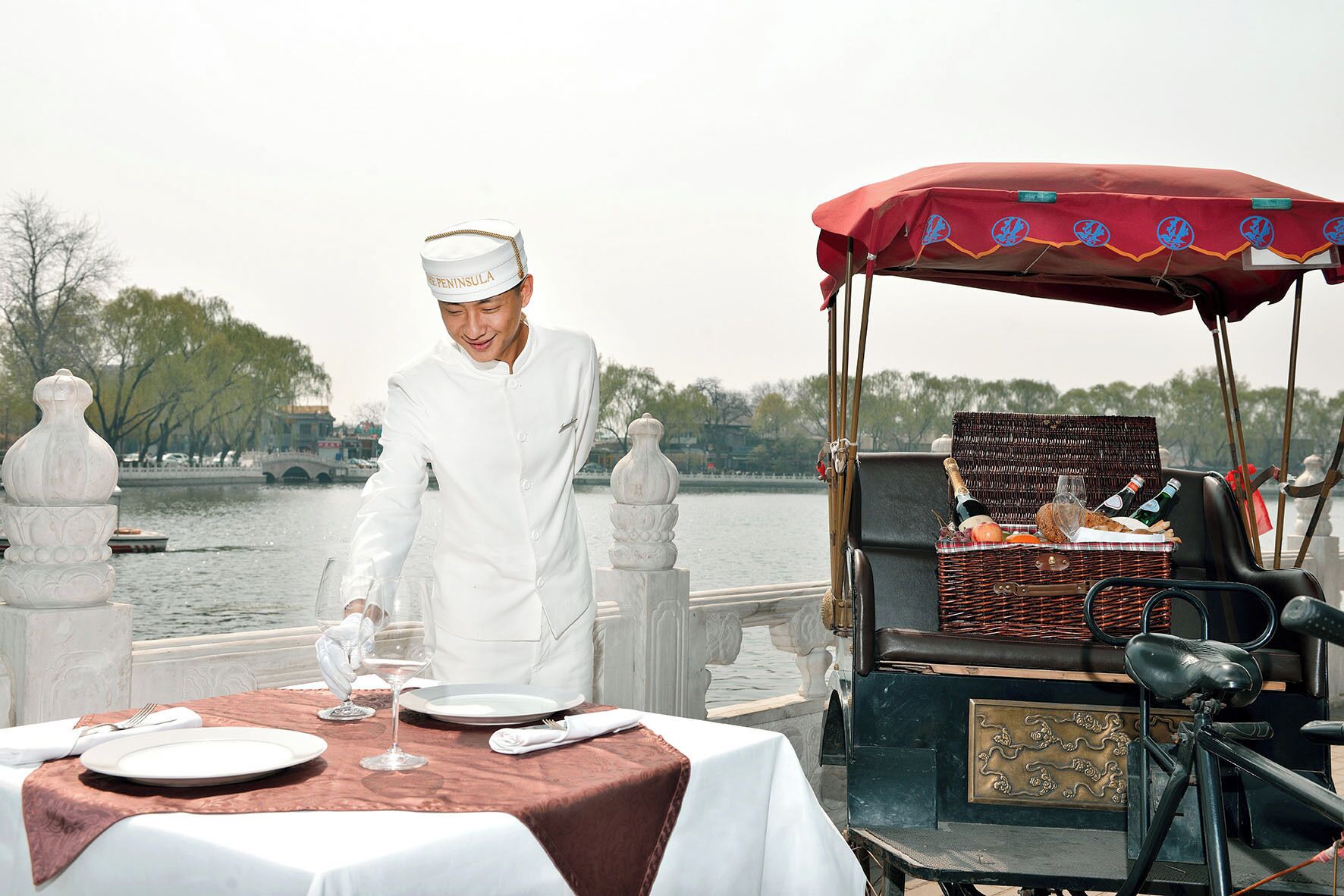 A table set for a meal with a wicker basket containing bottles and glasses, a red canopy, and a person in white attire.