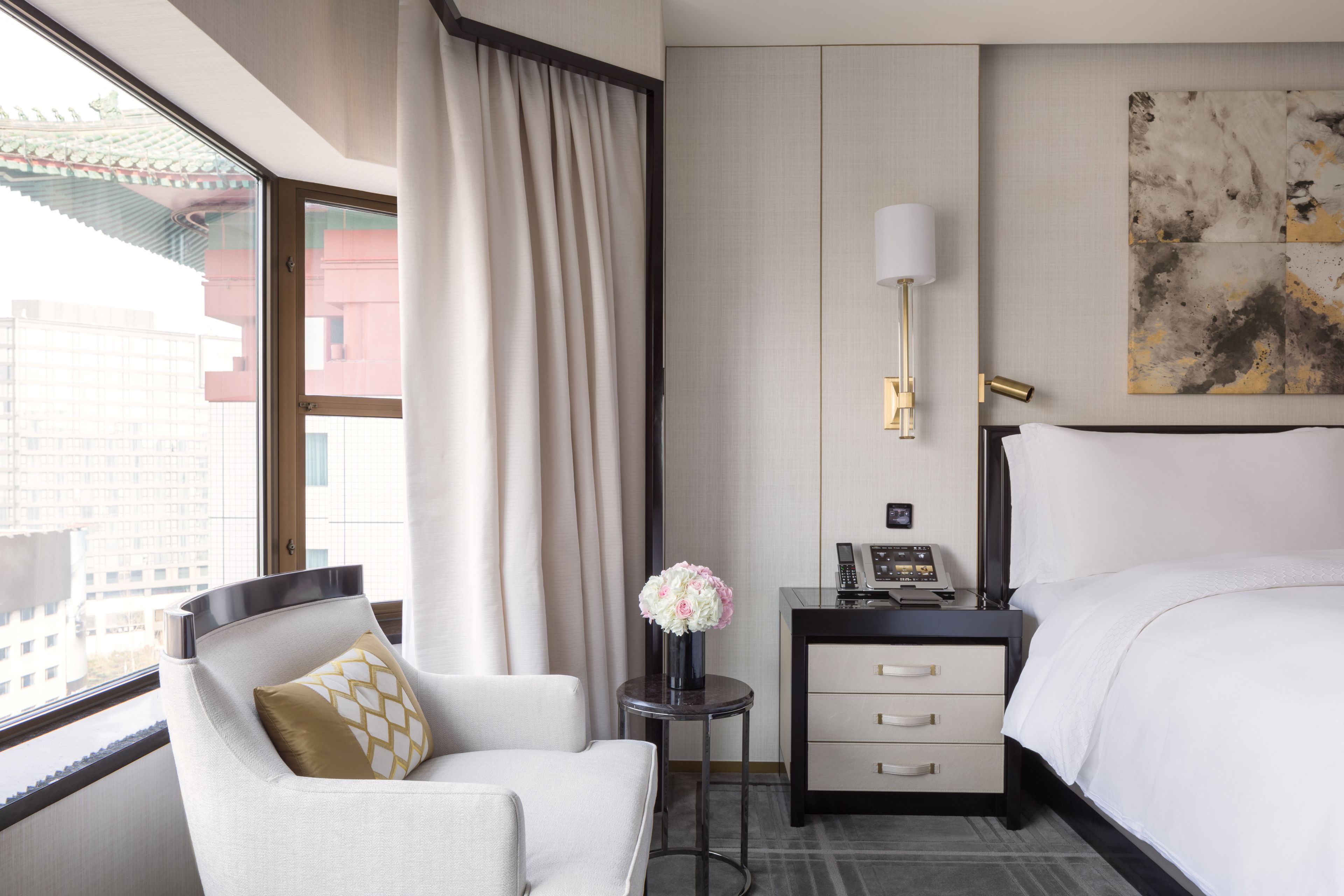 A hotel room with a bed, a desk with a lamp, a chair, and a vase of flowers.