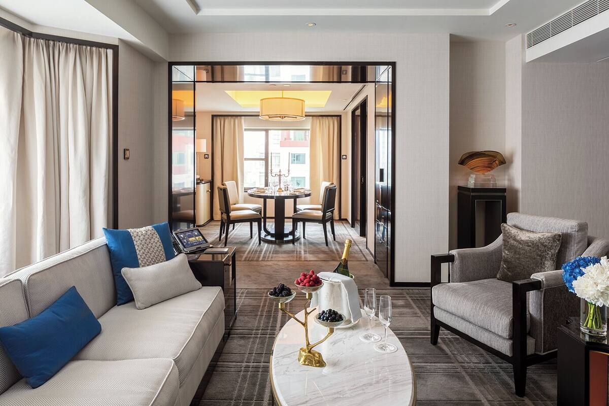 Una habitación de hotel moderna con sofá, sillón y zona de comedor con mesa y sillas.