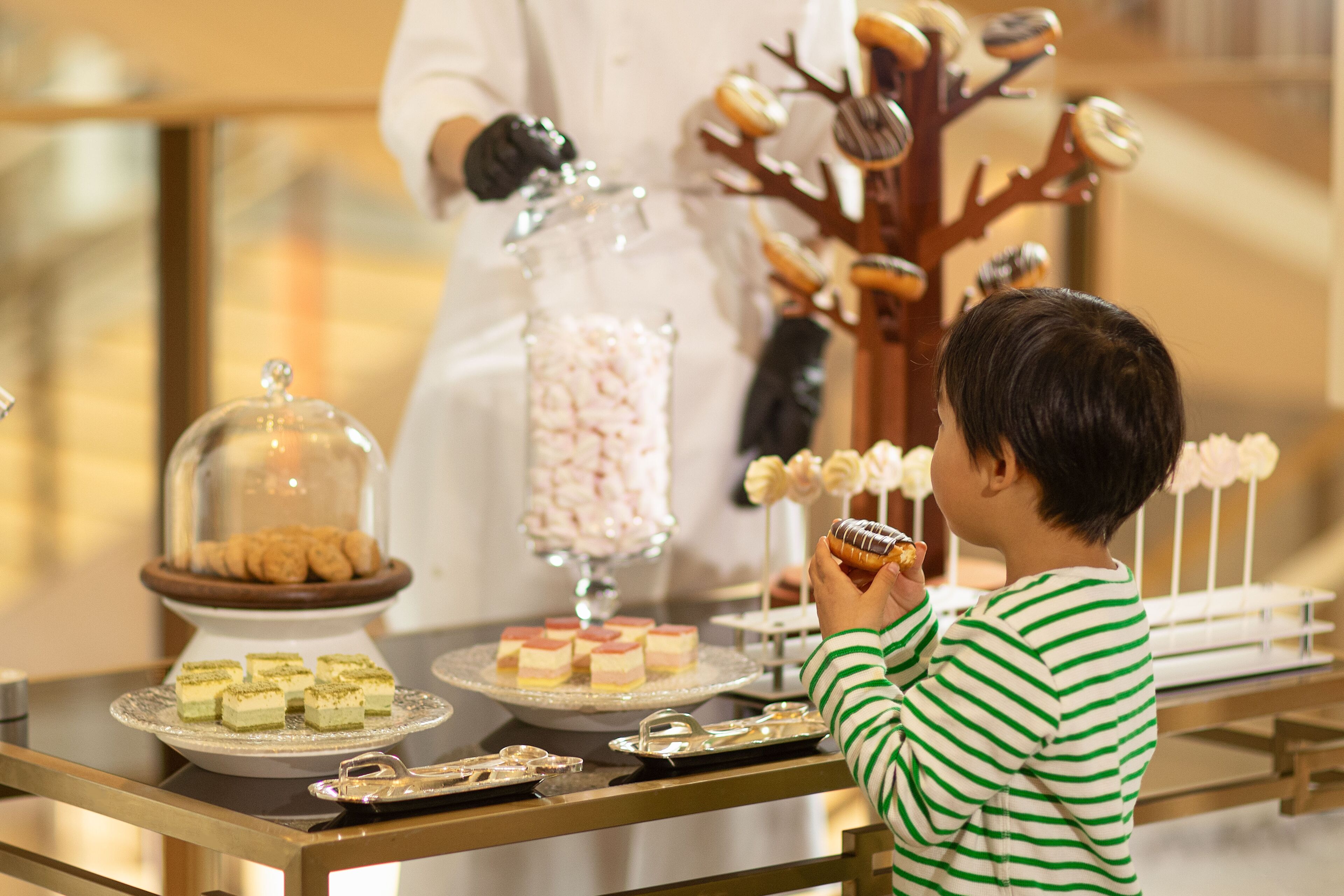 A table with various desserts and a child holding a donut.