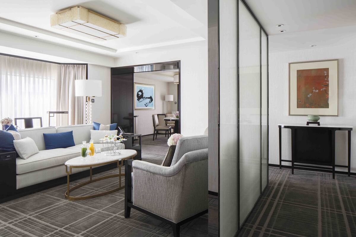 Una habitación de hotel moderna con sofá, sillón, mesa de centro y zona de comedor.