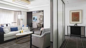 A modern hotel room with a sofa, armchair, coffee table, and a dining area.