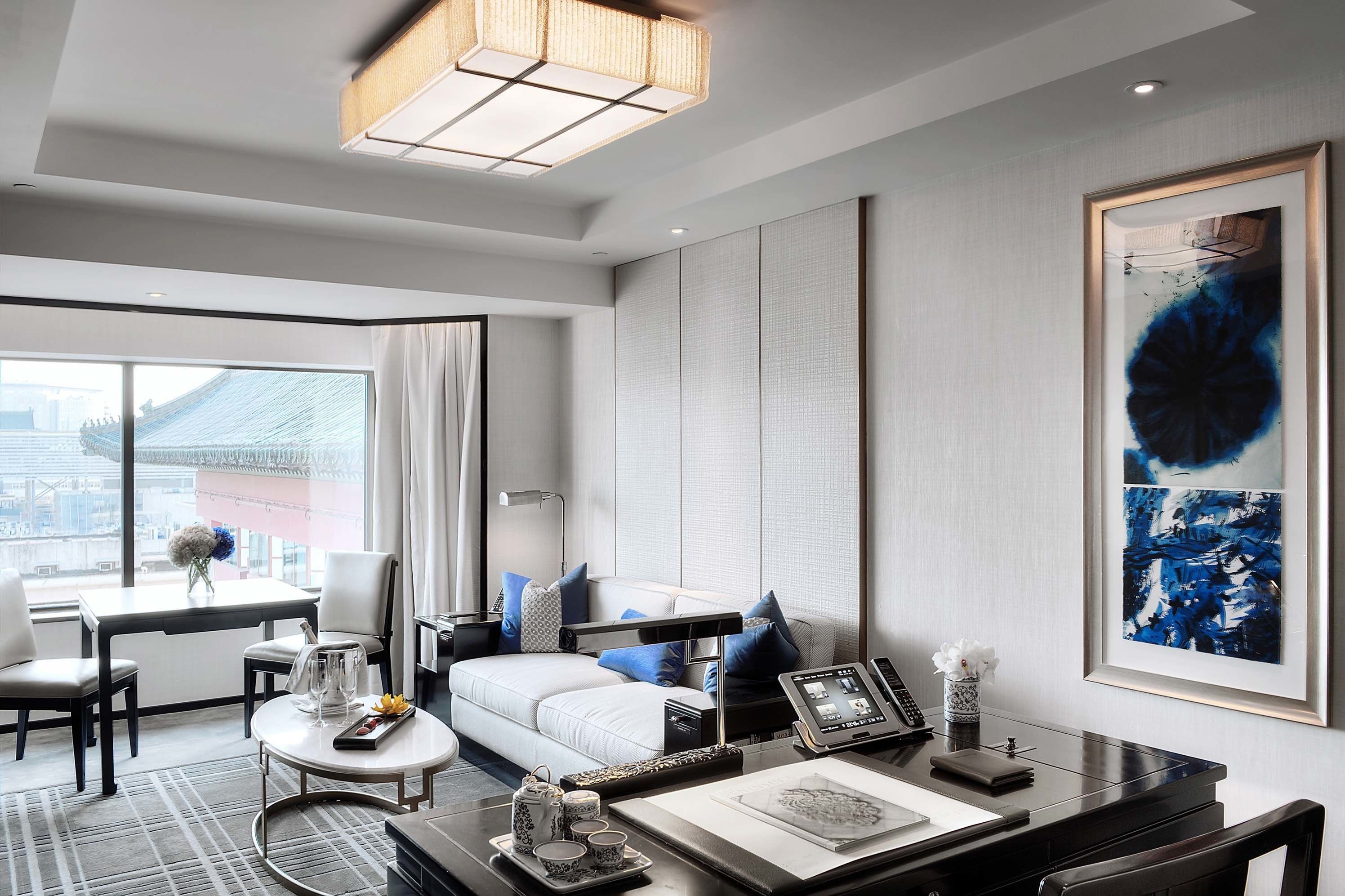 Una habitación de hotel moderna con un ventanal grande, un sofá, una mesa de comedor y un cuadro abstracto de gran tamaño.