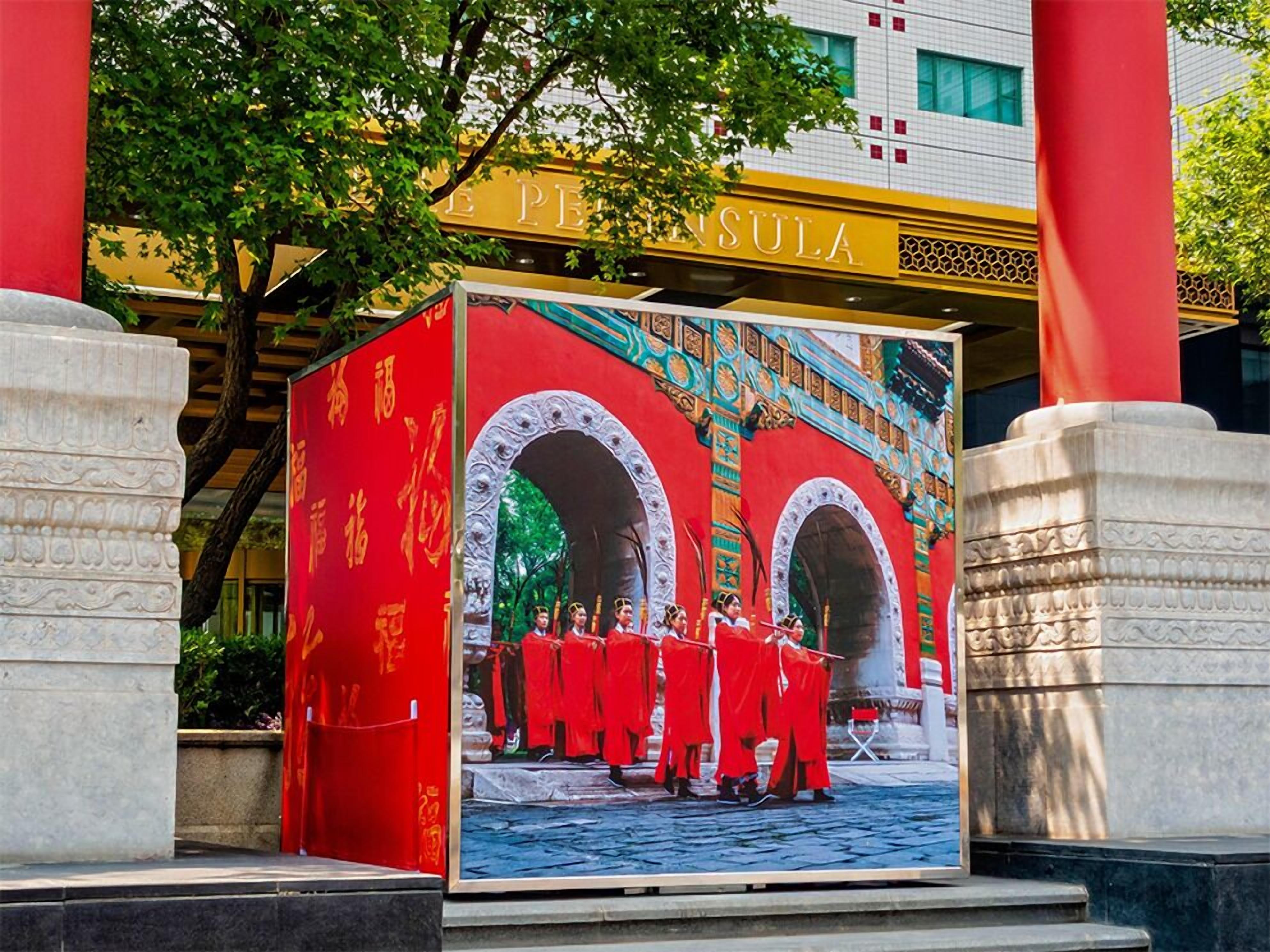 Fachada de prédio com um grande letreiro vermelho e dourado, uma escadaria e uma árvore ao primeiro plano.