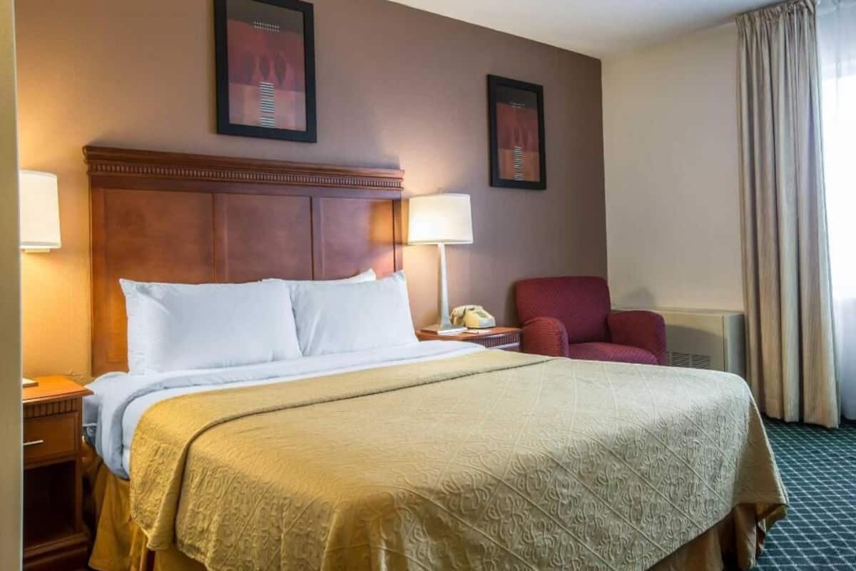 A hotel room with a large bed, two framed pictures on the wall, a red armchair, and a window with curtains.