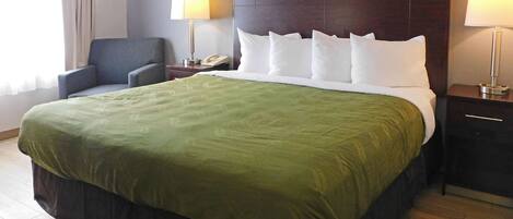 Una habitación de hotel con una cama grande, una mesita de noche, una silla y una lámpara.