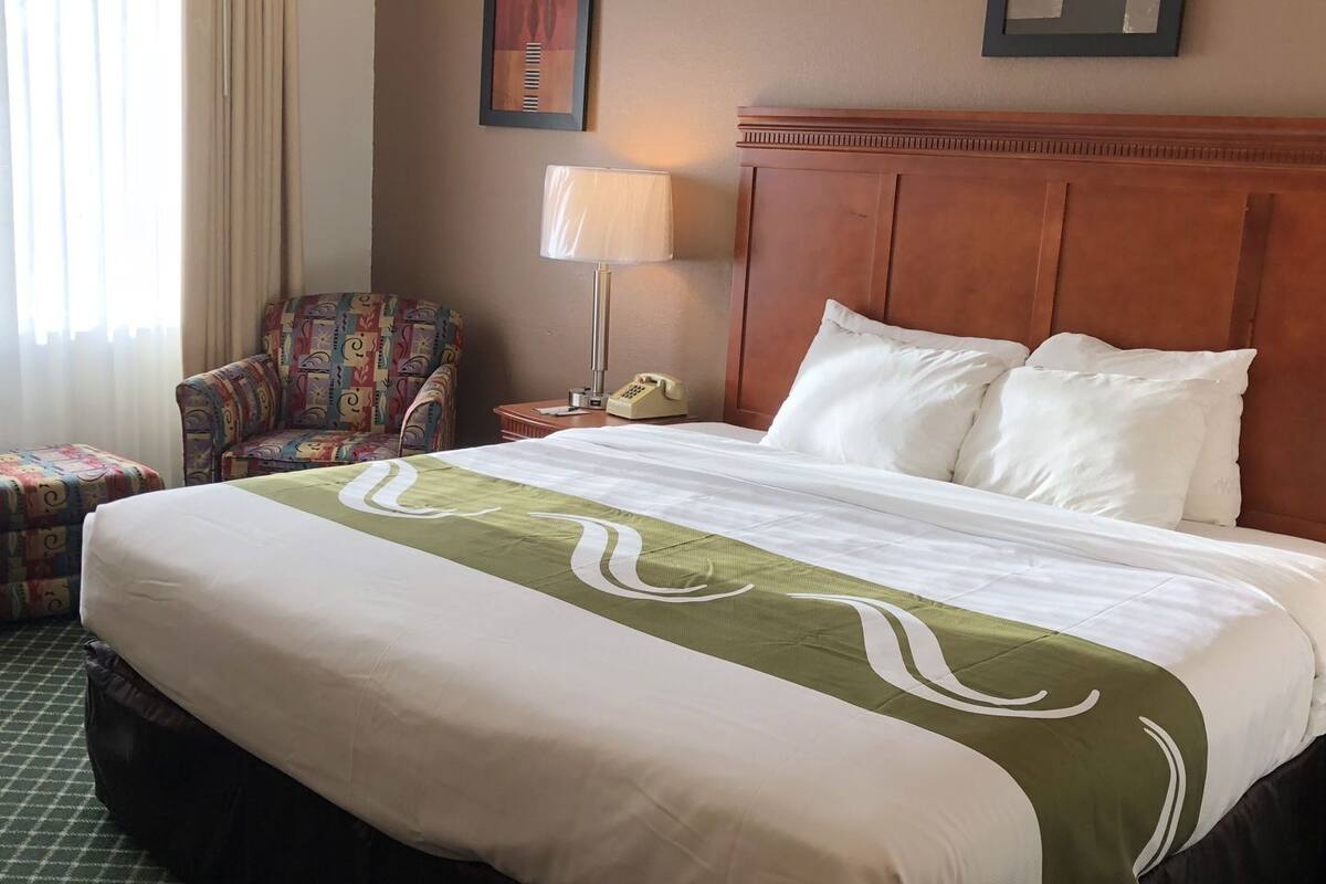 A hotel room with a large bed, a chair, a lamp, and a telephone.