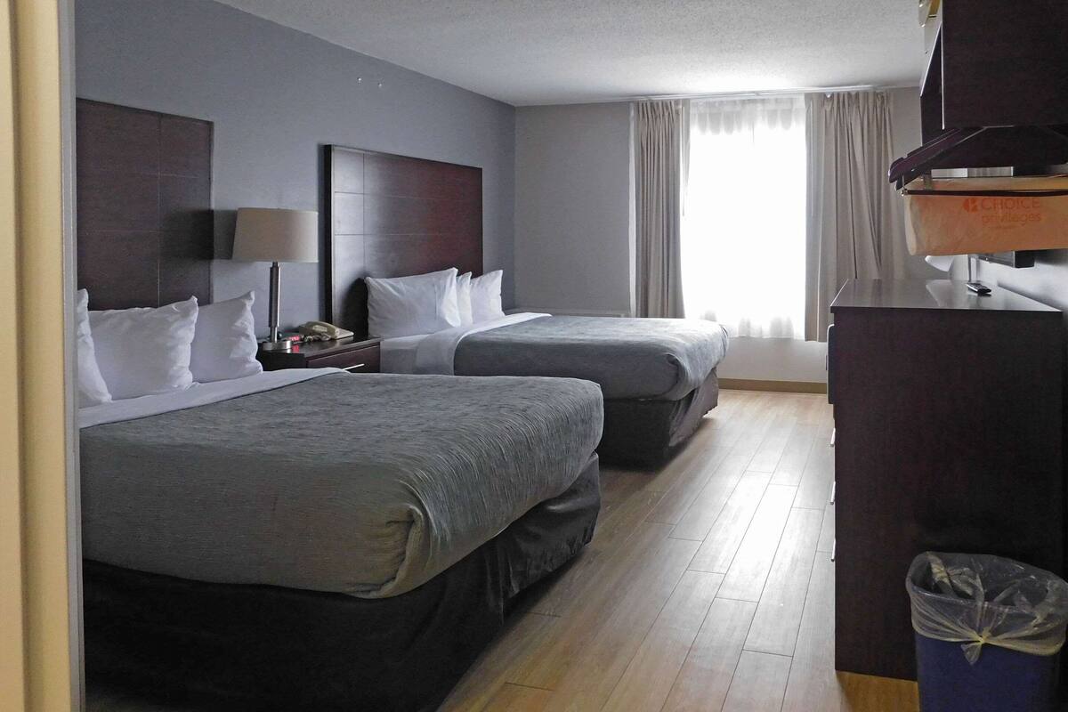 A hotel room with two beds, a desk, a trash bin, and a window with curtains.