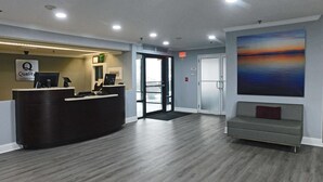 A hotel reception area with a reception desk, a waiting area with a bench, and a large painting on the wall. - Quality Inn Colchester - Burlington (Colchester)