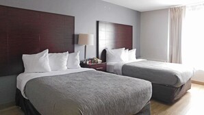 A hotel room with two beds, dark wood headboards, and a nightstand with a lamp. - Quality Inn Colchester - Burlington (Colchester)