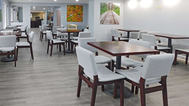 A modern dining area with multiple tables and chairs, a reception desk, and artwork on the walls. - Quality Inn Colchester - Burlington (Colchester)