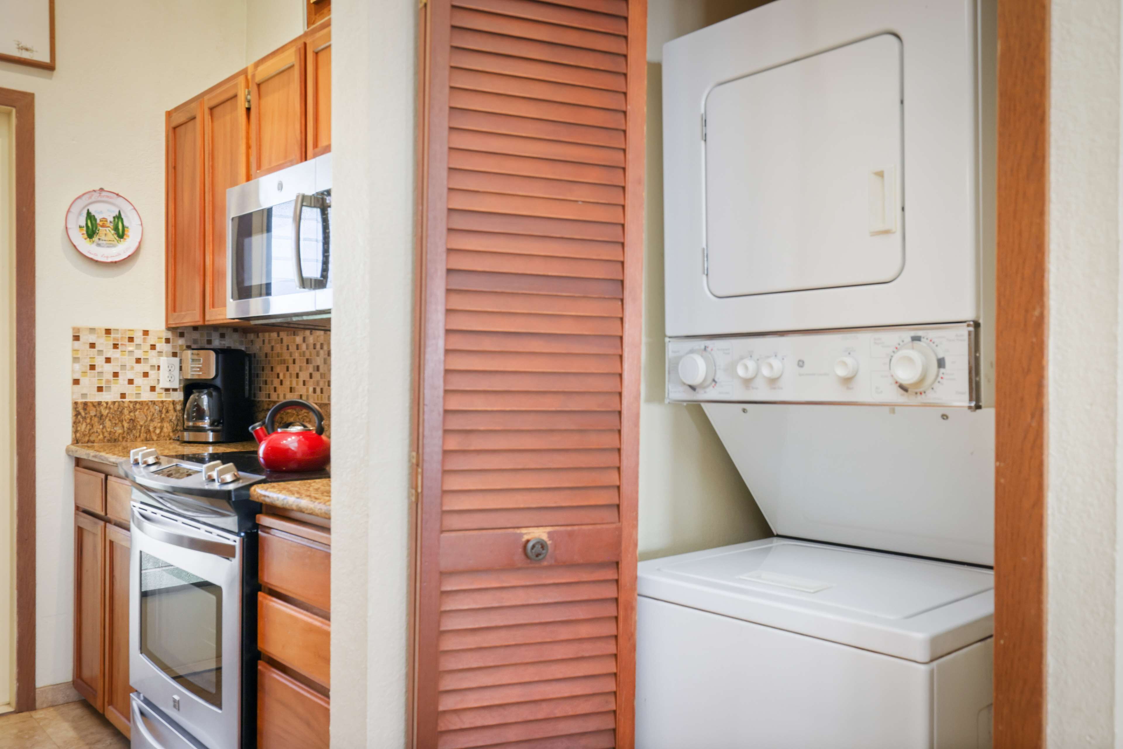 A compact kitchen with wooden cabinets, a stainless steel stove, a microwave, and a white washing machine.