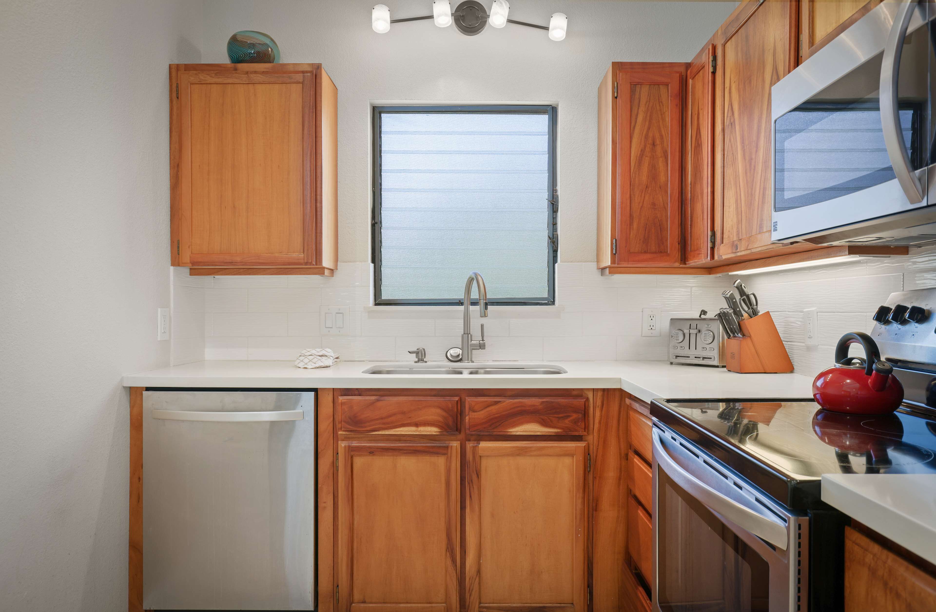 A kitchen with wooden cabinets, a stainless steel sink, a microwave, and a red kettle.