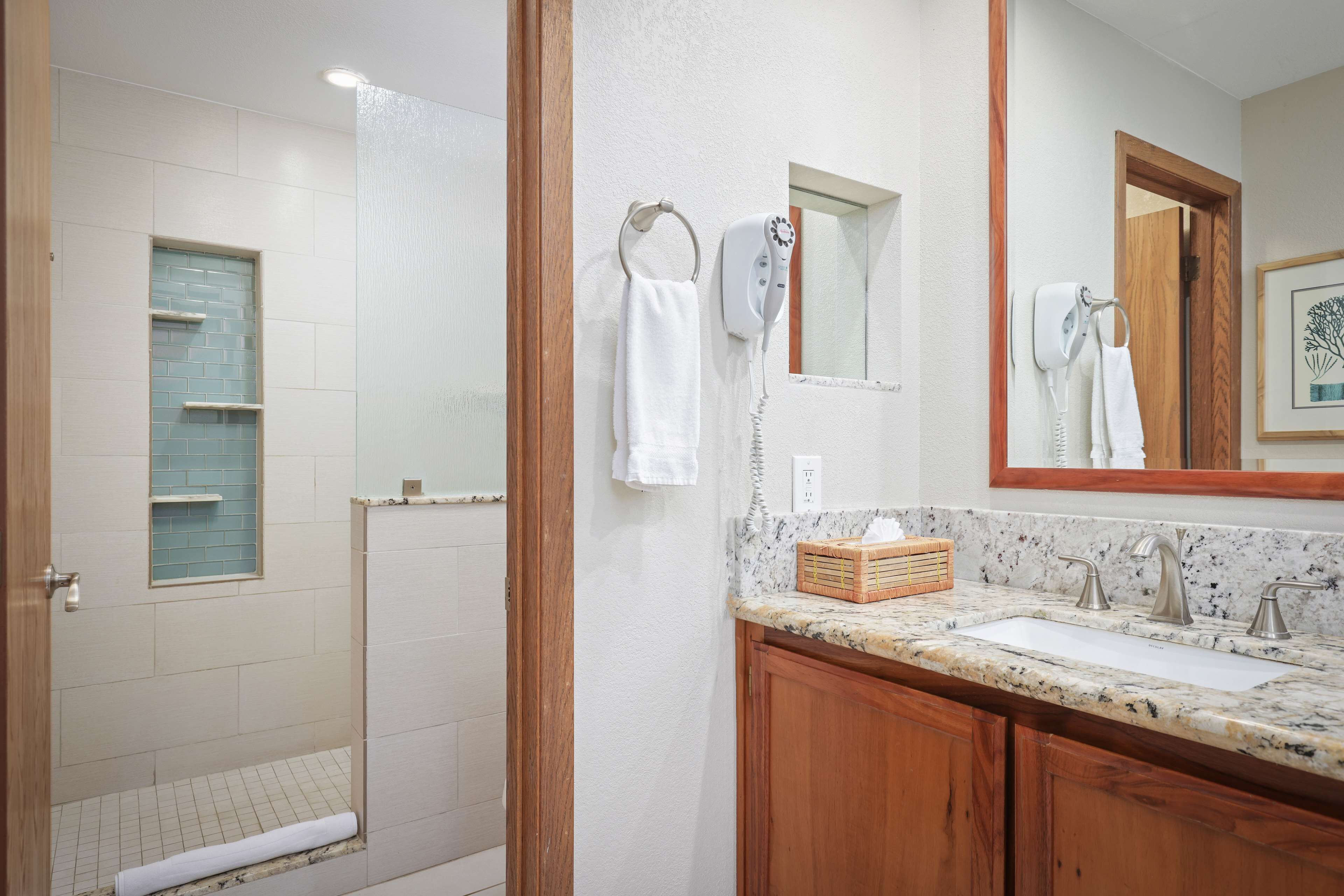 A bathroom with a shower, a sink with a marble countertop, and a wooden vanity.