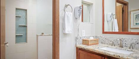 A bathroom with a shower, a sink with a marble countertop, and a wooden vanity.