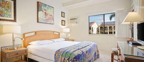 A hotel room with a bed, a desk, a chair, a ceiling fan, and artwork on the walls.