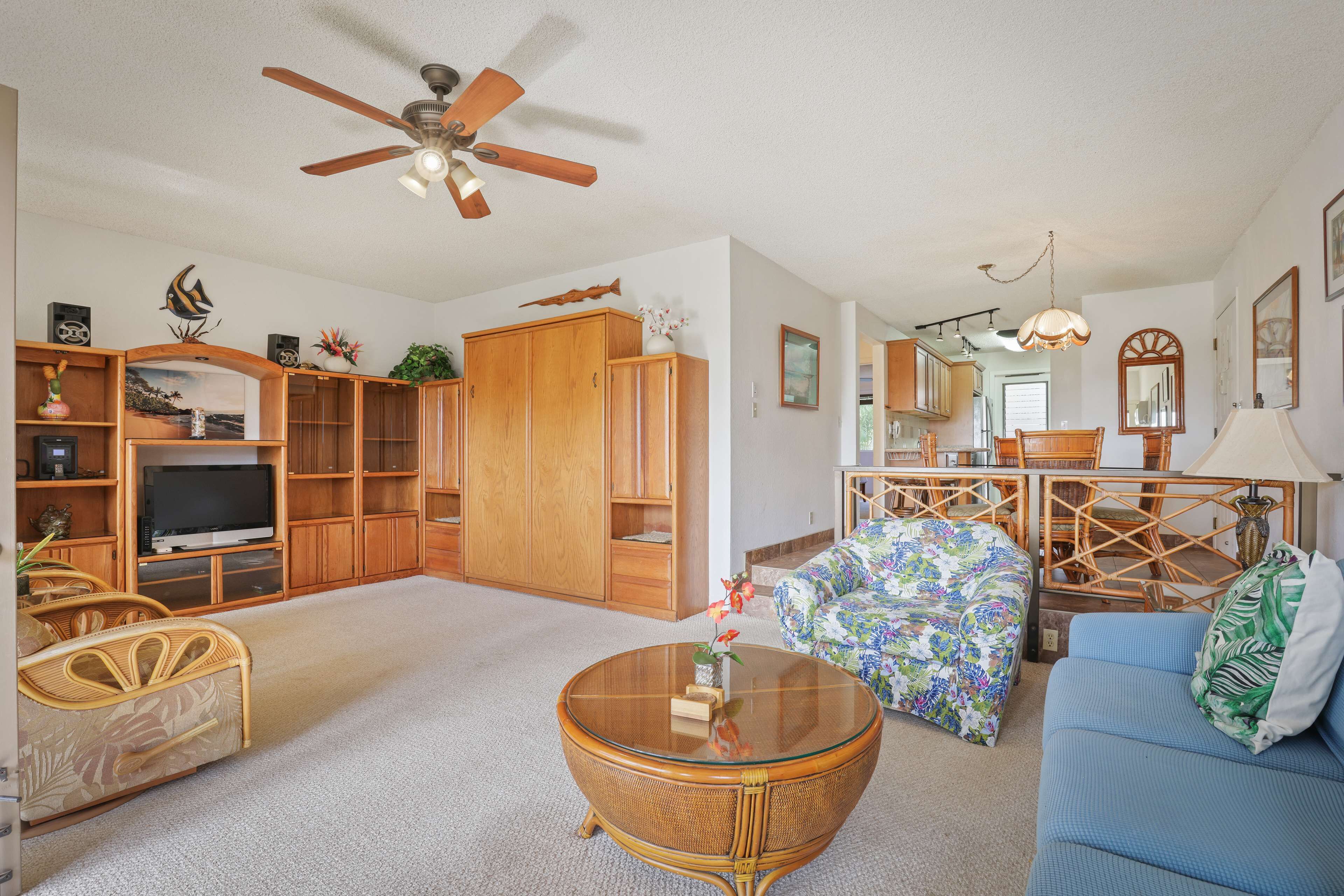 A spacious living room with a television, wooden cabinets, a round glass coffee table, and a blue sofa.