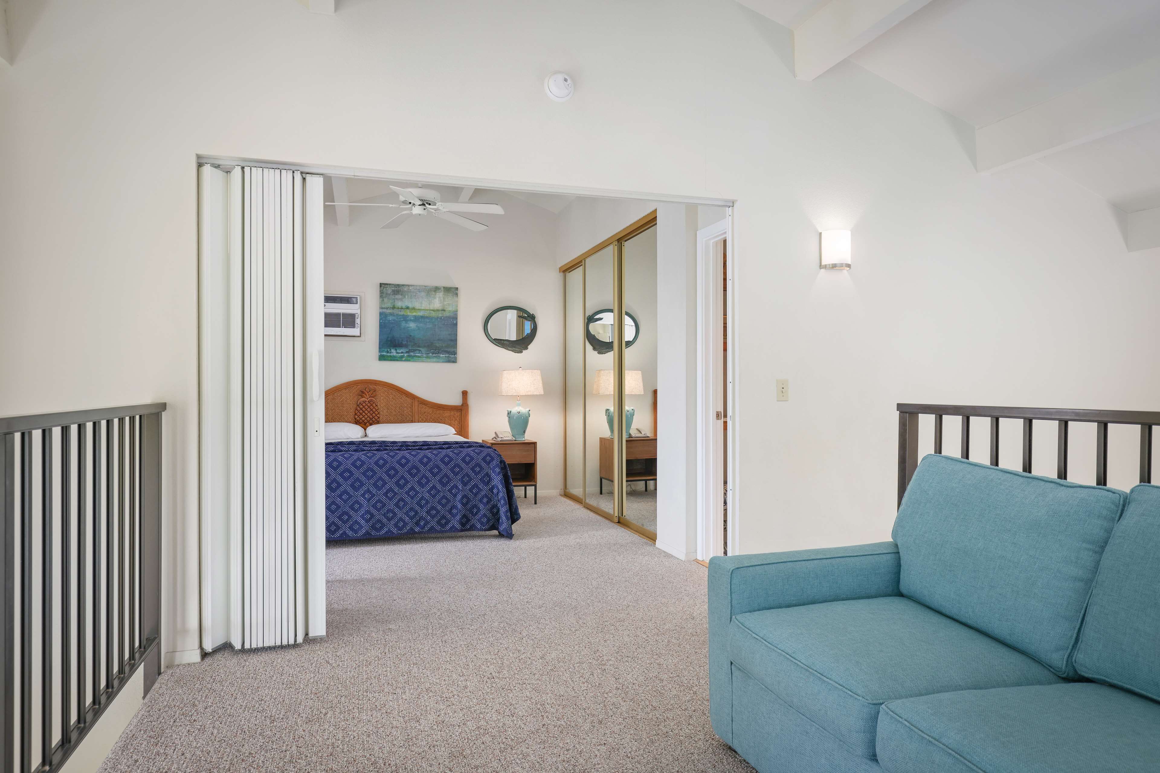 A bedroom with a bed, a blue sofa, a ceiling fan, and a mirror.