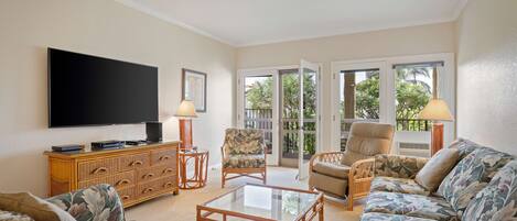 A living room with a flat-screen TV, wicker furniture, a glass coffee table, and a ceiling fan.