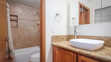 Un baño con lavamanos blanco, armarios de madera, ducha e inodoro.