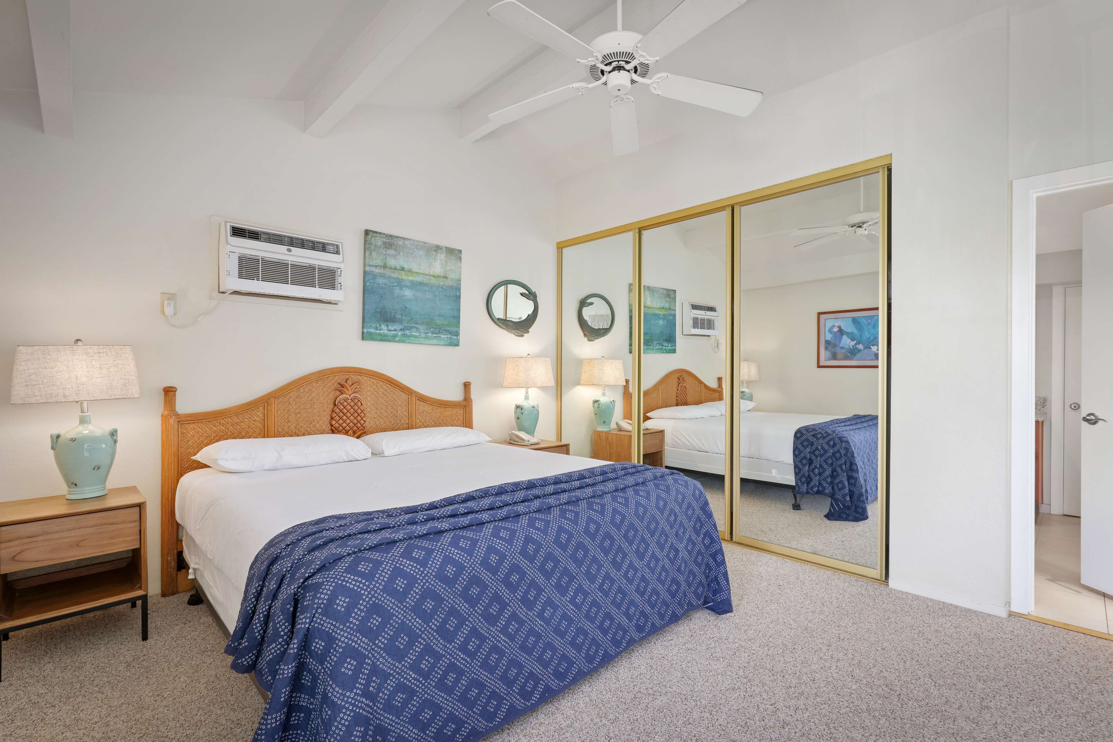 A bedroom with a large bed, a ceiling fan, a wardrobe, and a mirror.