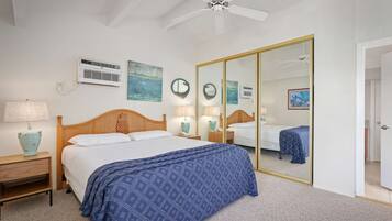 A bedroom with a large bed, a ceiling fan, a wardrobe, and a mirror.
