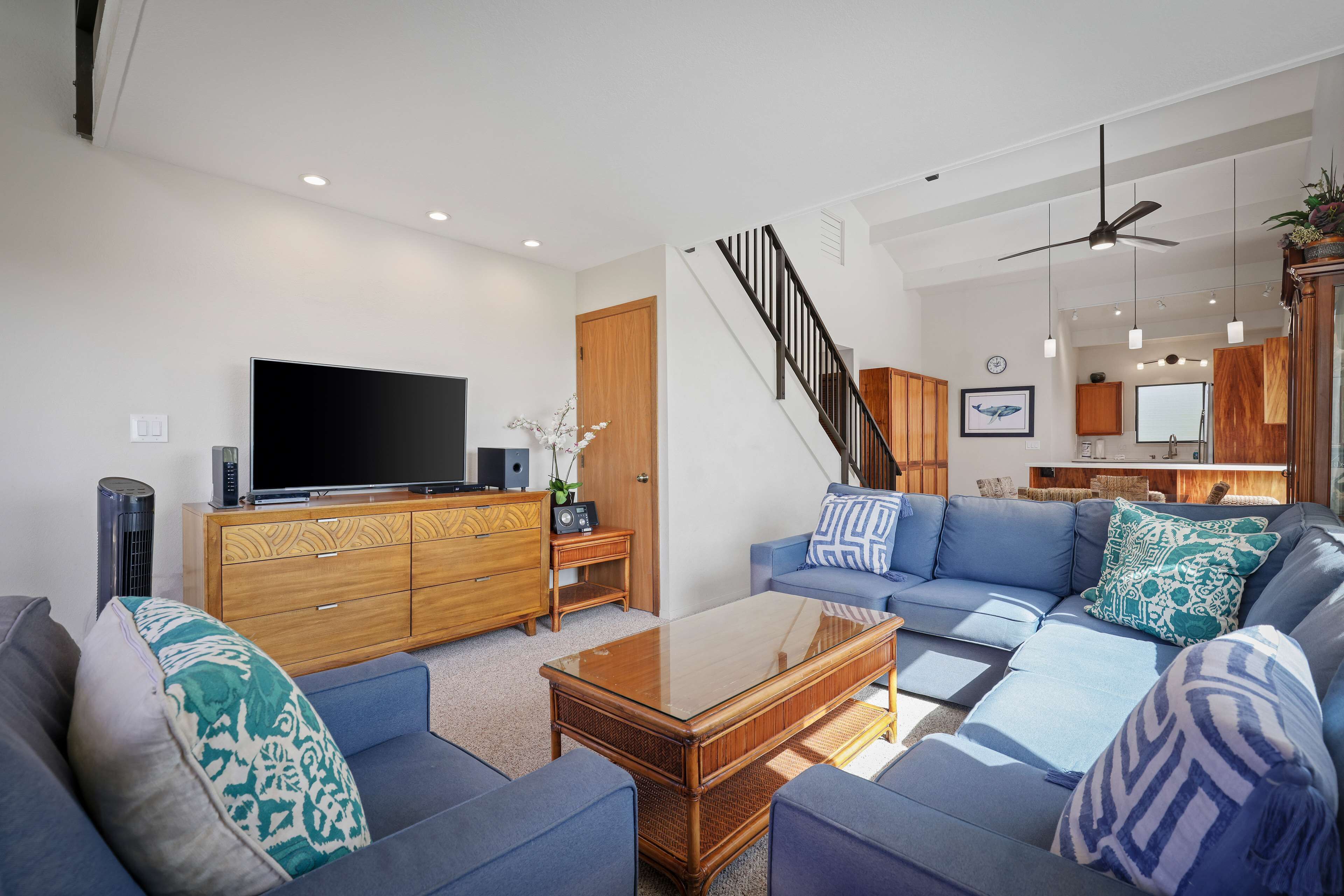 A modern living room with a flat-screen TV, a wooden cabinet, a blue sofa set, and a staircase.