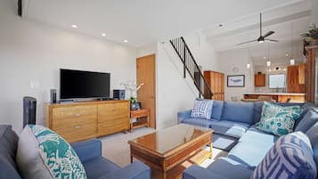 A modern living room with a flat-screen TV, a wooden cabinet, a blue sofa set, and a staircase.