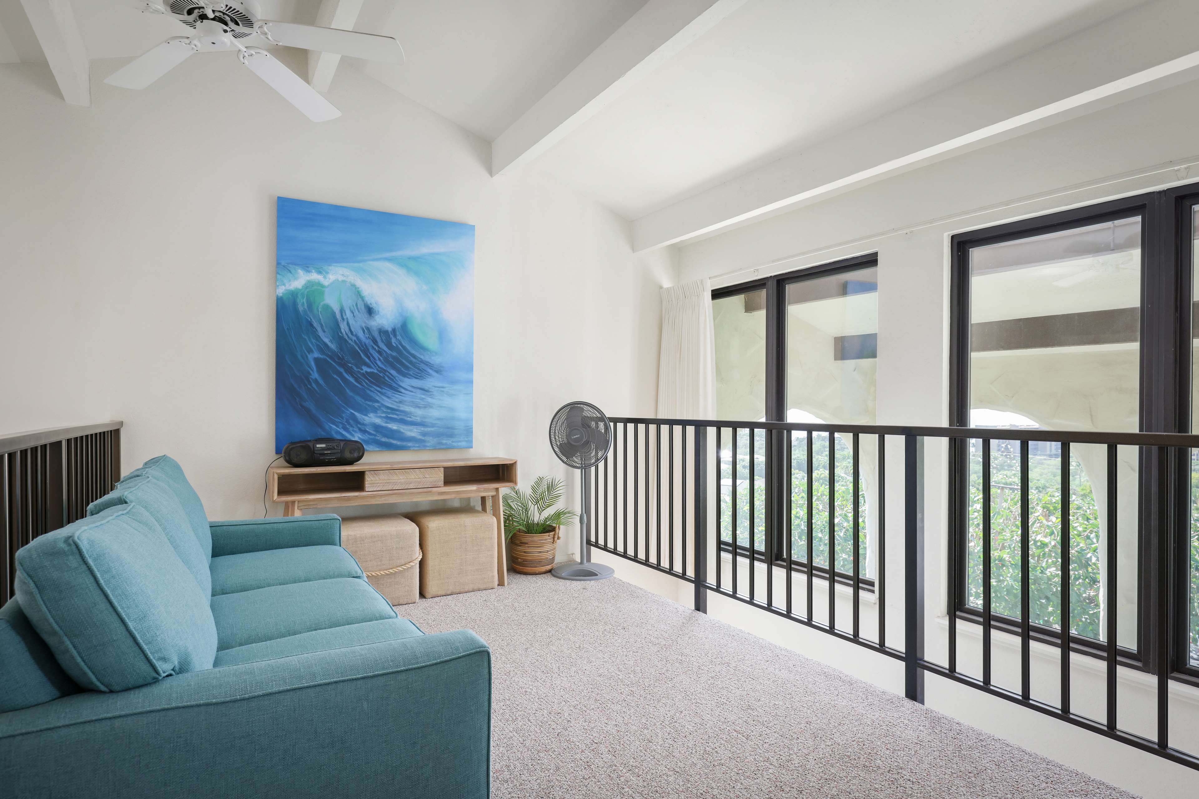 A balcony with a view of greenery, a ceiling fan, and a large wave painting on the wall.