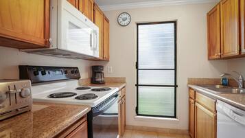 Une cuisine avec des meubles de rangement en bois, un four blanc, un four à micro-ondes et une horloge au mur.
