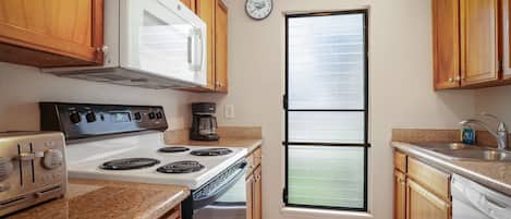A kitchen with wooden cabinets, a white stove, a microwave, and a clock on the wall.
